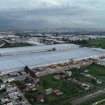Aerial view of industrial warehouses in Mexico City surrounded by residential areas and greenery.